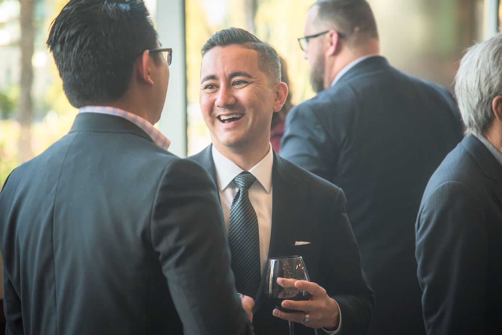 Professionals in suits networking at a leadership mixer — candid moment of connection during a civic or corporate event, captured with warmth and clarity.